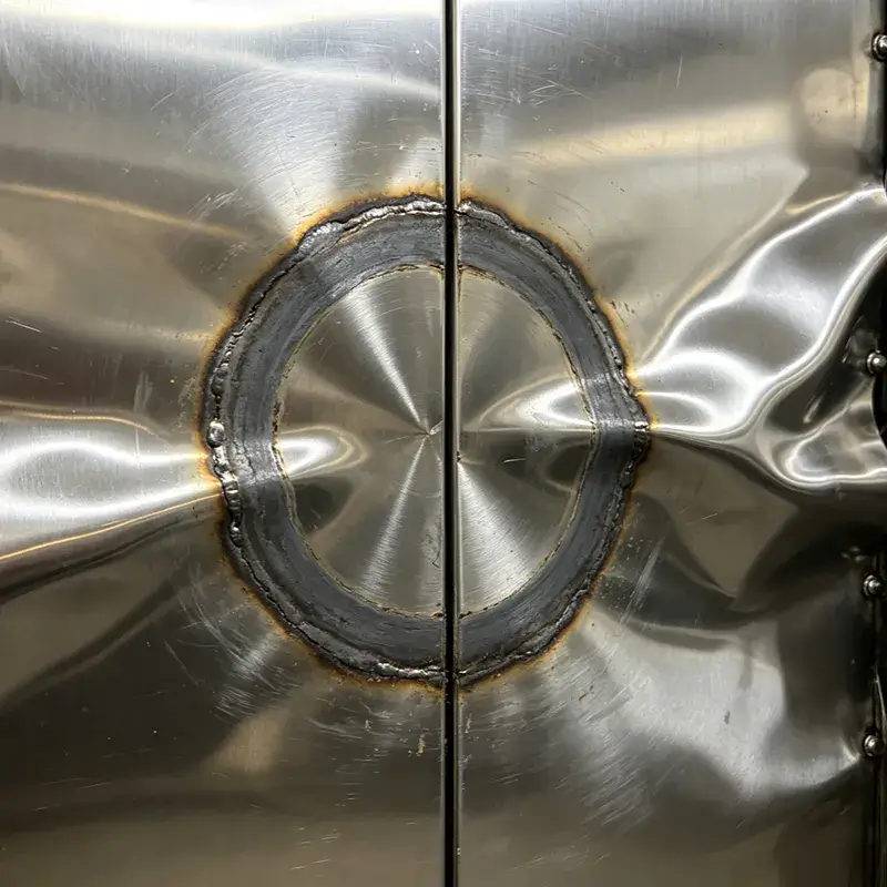 Thermal read-through and warping defects on the decorative face of a stainless steel elevator panel caused by arc welding stiffeners.
